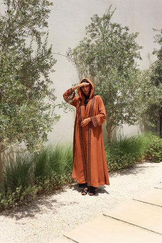 The Language Of Flowers S.FO8, a captivating rust abaya adorned with elegant black leaf embroidery flowing gracefully along the front and sleeves.