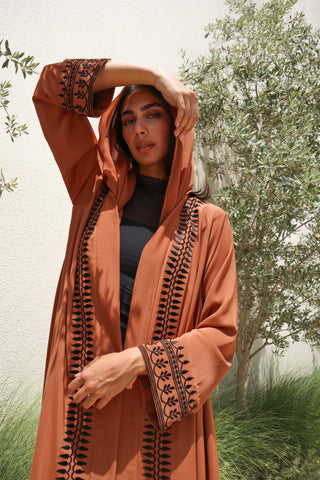 The Language Of Flowers S.FO8, a captivating rust abaya adorned with elegant black leaf embroidery flowing gracefully along the front and sleeves.