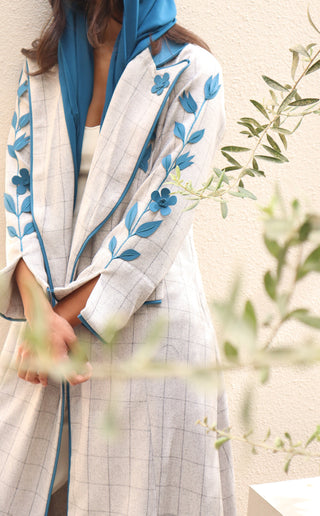 Shimmer-The Art of Layers S.LO1 - a luxurious grey check abaya adorned with intricately cut leather floral motifs, beautifully layered across the design and finished with refined blue piping.
