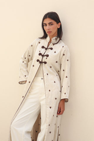 Letters From Kyoto S.KO5 is a refined ivory printed abaya featuring delicate brown piping and elegant knot buttons. 