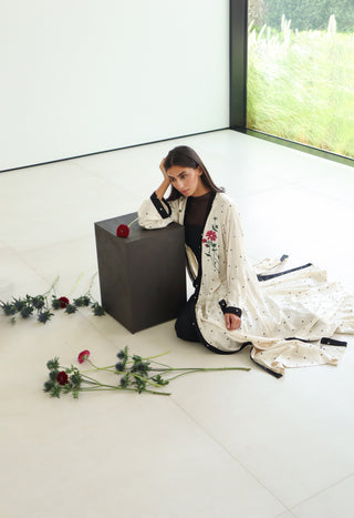 An elegant ivory abaya adorned with delicate floral embroidery and defined by refined black trim.