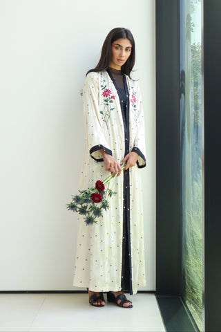 An elegant ivory abaya adorned with delicate floral embroidery and defined by refined black trim.