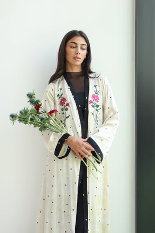 An elegant ivory abaya adorned with delicate floral embroidery and defined by refined black trim.