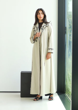 The Art of Layers S.LO11 - luxurious ivory striped abaya adorned with intricate black floral embroidery and refined piping details. 