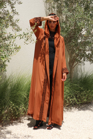 The Language Of Flowers S.FO8, a captivating rust abaya adorned with elegant black leaf embroidery flowing gracefully along the front and sleeves.